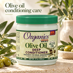 A jar of Organics by Afters Best Olive Oil Deep Conditioner is shown on a stone surface with olive branches and olives around it. The product jar has a green lid and a cream-colored label with green and purple text.