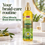 A bottle of African Pride Olive Miracle Braid Sheen Spray stands on a marble countertop in a bright bathroom setting with towels, a soap dish with olives, and gold fixtures. Large promotional text on the left reads, 'Your braid-care routine' and 'Olive Miracle Braid Sheen Spray.