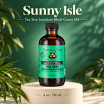 A bottle of Sunny Isle Tea Tree Jamaican Black Castor Oil stands on a round pedestal against a green leafy background. The amber glass bottle has a black cap and a bright green label with black text.